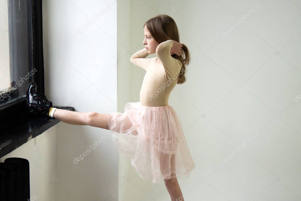 Teenage girl in a bodysuit and a fluffy tulle pink skirt looks out the window