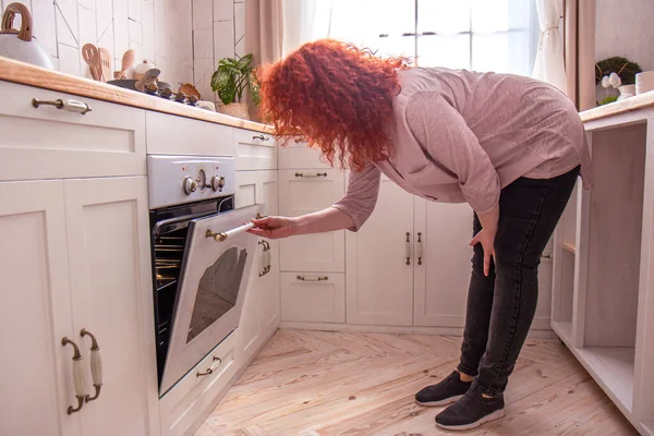 Mujer mira en el horno en la cocina por la mañana — Foto de Stock