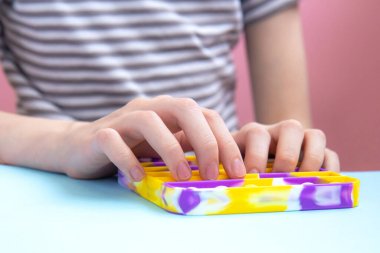 Günlük giysili çocuk, parlak renkli anti-stres oyuncağıyla oynuyor. Boş pembe arka planda yeni oyuncaklar. Kapat.
