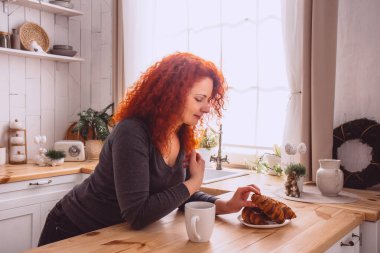 Genç ve mutlu bir kadın sabahları mutfakta kahve içiyor.