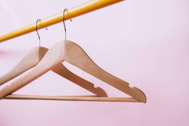 İki ahşap elbise askısı pembe arka planda sarı bir askıda asılı.