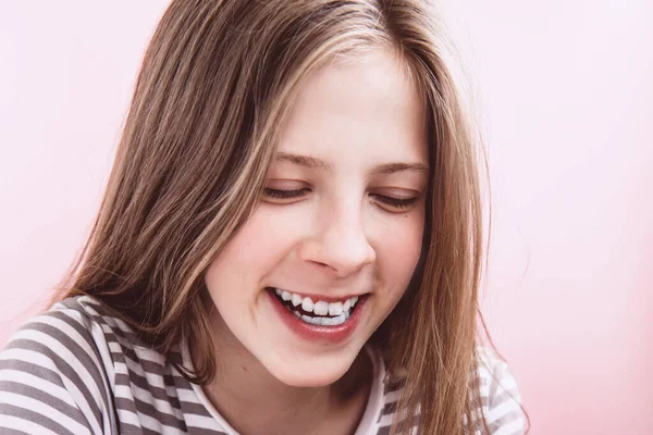Tvář krásné usmívající se dospívající dívka s dlouhými vlasy na růžovém pozadí — Stock fotografie