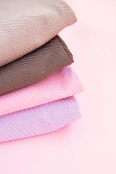 Colorful cotton folded clothes stack. Stack of multicolored clothes on pink background. Set of clothes in nude colors