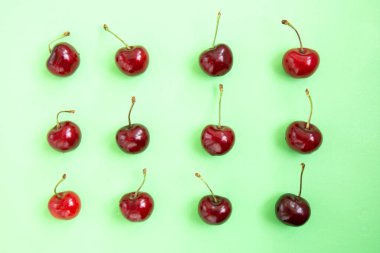 Yeşil arka planda satranç tahtası deseninde parlak kırmızı kiraz. Kiraz deseni. Kirazlar kapanıyor. Yaz yassı böğürtlen arka planı. Geometrik desen. Üst görünüm