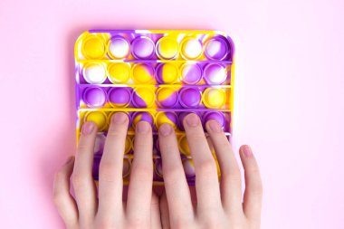 Parlak renkli anti-stres oyuncağı olan çocuk, patlat şunu. Boş pembe arka planda yeni oyuncaklar. Kapat.