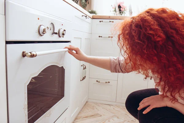 Mujer mira en el horno en la cocina por la mañana — Foto de Stock