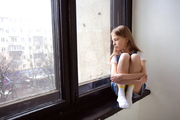 Teenage girl with long blond hair looks out the window — Stock Photo, Image