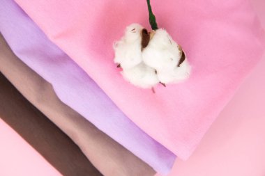 Renkli pamuklu katlanmış kıyafet yığını. ve pamuk filizi. Pembe arka planda bir sürü renkli kıyafet var. Çıplak renkte giysiler.