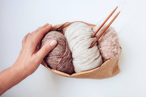 Woman's hand holds a craft eco bag with skeins of yarn in nude colors and knitting needles on a white background. Copy space. Knitwear as a concept of female hobby. Front view