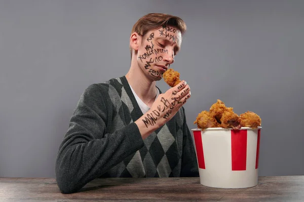 Üzgün bir adam tavuk budu tutuyor ve ona bakıyor. Abur cubur yemesi gerekip gerekmediği konusunda endişeleniyor.