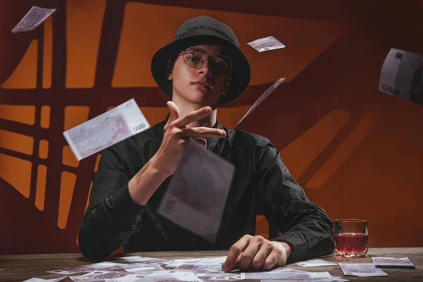 Havalı adam sırıtıyor ve kameraya para atıyor.