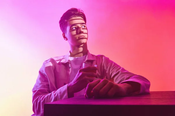 Bir bardak viskiyle turuncu-mor arka planda bir adam.