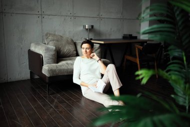 Bir kadın oturma odasında yerde otururken bir kitap okuyor. Evde sakin bir gün