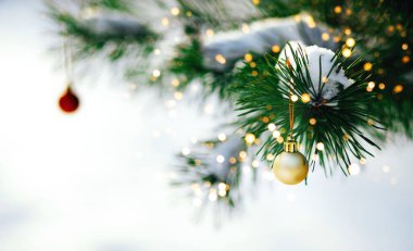 Yılbaşı ağacının dalları, karlı arka planda ışıklar ve sarı top.