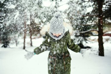 Bir kız ağaçların altında duruyor, kar yağıyor, temiz havada eğlenceli bir oyun.