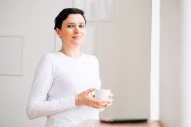 Pencerenin yanında bir kadın duruyor.