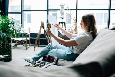 Genç bir kadın hafif bir stüdyoda çizim yapıyor.