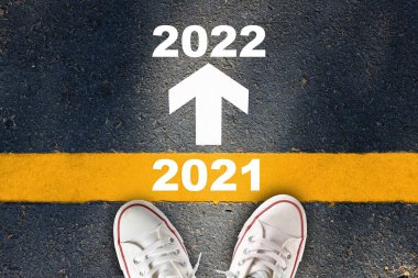 2021 'den 2022' ye kadar yeni yıl ve asfalt yolda sarı çizgili beyaz ok işareti. Ticari mücadele kavramı ve yön fikriyle denemeye devam edin