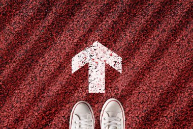 Beyaz spor ayakkabı ya da kırmızı yol arka planında ok olan spor ayakkabı. Devam et konsept ve devam et.