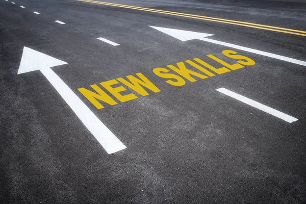New skills word and yellow arrow on asphalt road with marking lines for separate lane. Reskilling and upskilling development concept and changing skill demand idea