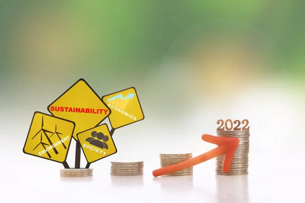 New year 2022, environment, society and economics written on yellow sign on stack of coins with red arrow upwards on abstract background. Sustainable with return on investment concept and economic growth idea