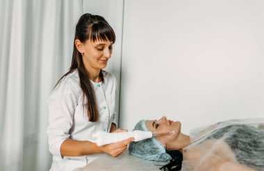 Yüzün Darsonvalizasyonu ya da elektroterapi yardımıyla yüzün gençleşmesi. Darsonval 'ın yüzü için bir fotoğraf. Şu anki terapi. Hasta güzellik uzmanında.