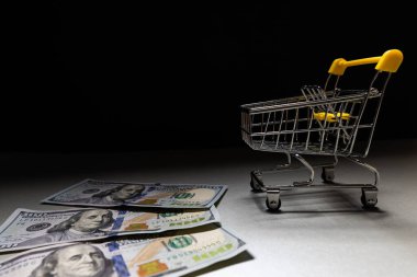 Bir süpermarkette arka planda minyatür bir alışveriş arabasının yanında birkaç yüz dolarlık banknot yatıyor. Metin için yer