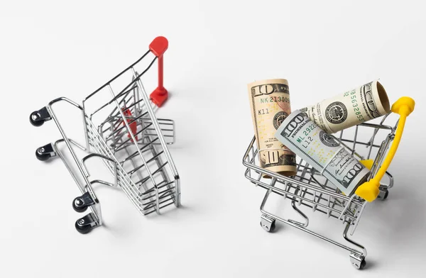 Dolarlı alışveriş arabası beyaz arka planda duruyor ve yanında boş bir alışveriş arabası yatıyor..