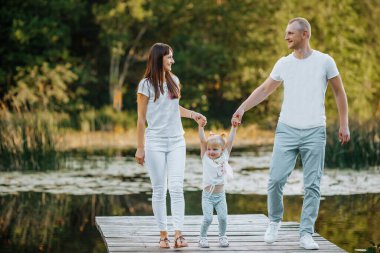 Mutlu genç aile gölde ya da nehirde eğleniyor, gün batımında koşup zıplıyor.