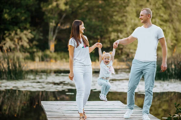 Genç ve mutlu bir aile göl kenarında el ele yürürken sokakta birlikte vakit geçiriyorlar.