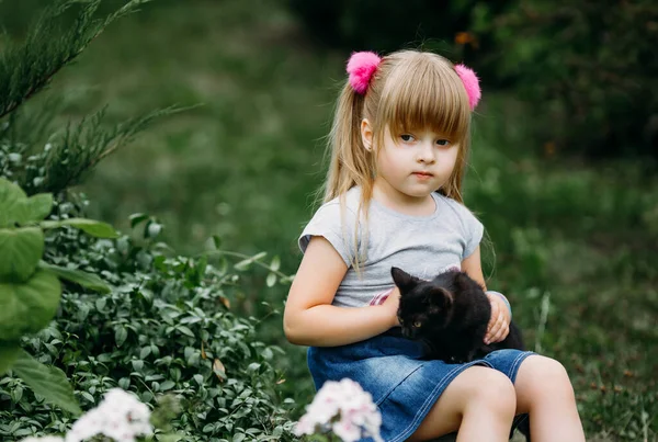Kucağında siyah bir kedi yavrusu olan küçük tatlı bir kız. En iyi arkadaşlar. Çocukların evcil hayvanlarla etkileşimi.