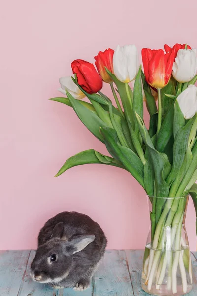 Vazoda bir buket lale olan pembe arka planda küçük şirin bir tavşan.