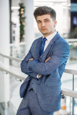 Mavi takım elbiseli ve mavi kravatlı bir iş adamının kameraya bakarken çekilmiş dikey fotoğrafı..