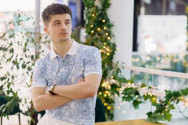 Conceptual photography of wealthy people living a luxurious life. Young successful elegant businessman stands in a cafe with folded hands.