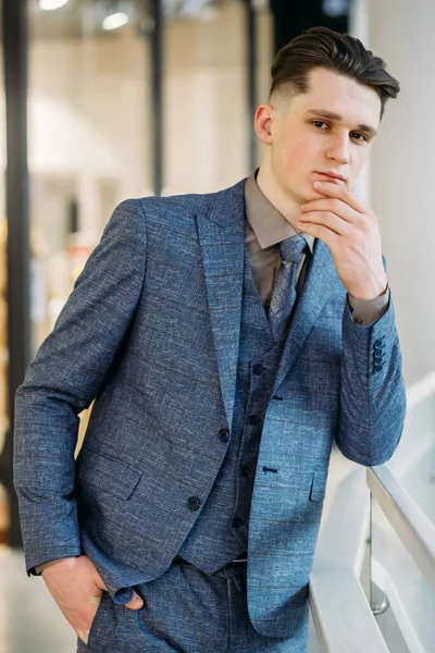 Modern style. Young man in blue suit and tie holding chin and looking at camera
