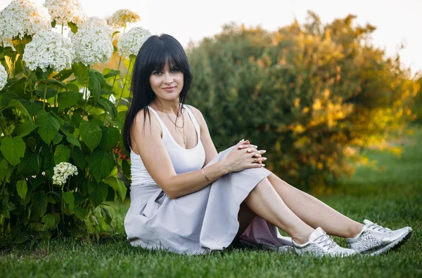 A beautiful young girl is sitting among the flowering bushes. White flowers. Spring. Girl with hair in a white T-shirt. Portrait. Romance.