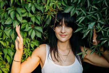 Sarmaşık içinde, dışarıdaki yaz parkında güzel bir esmerin portresi.