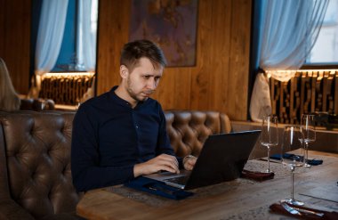 Restoranda bir masada oturup dizüstü bilgisayarla çalışan serbest çalışan bir adamın portresi..