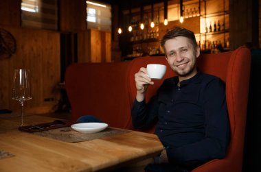 Yakışıklı genç adam bir restoranda ya da kafede kahve içiyor ve kameraya gülümsüyor. Bir istemci veya bileşenle toplantı bekleniyor.