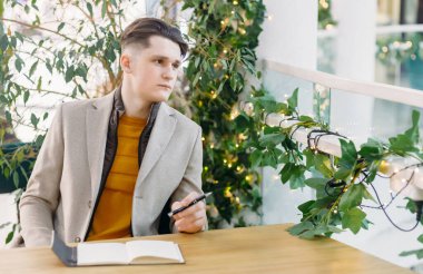 Kafede ya da restoranda çalışan bir adam. Elinde bir kalem tutuyor ve yan tarafına bakıyor, periyodik olarak bir deftere not alıyor. Koronavirüs sırasında sosyal mesafeler.