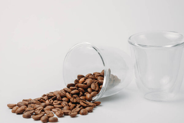 coffee beans spilling out from a glass cup on a white background. Two glass espresso cups. Place for text.