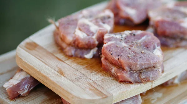 Råkött på en träskiva, styckat i bitar, kryddat och färdigt att grilla utomhus på bakgrunden. Närbild, hälsosam mat — Stockfoto