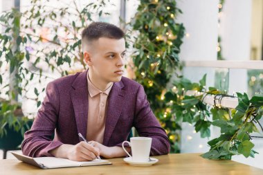 Şirin genç işadamı, elinde bir kalem ve defterle bir kafede otururken gününü planlıyor.