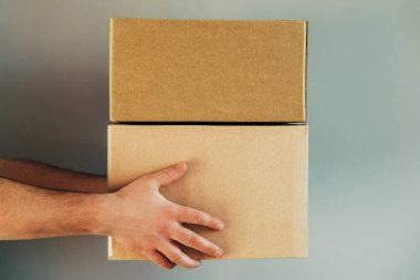 Teslimatçı adamın elleri gri arka planda karton kutular teslim eder. Teslimat hizmeti, online alışveriş ve lojistik konsept.