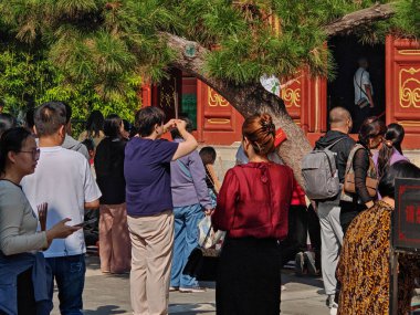 Sep 24 2025 - Pekin, Çin: Pekin 'deki Yonghegong Lama Tapınağı' nda canlı bir sahne, kalabalık bir şehir ortamında elinde siyah bir joss çubuğu tutan bir kadınla geleneksel bir dini tören yapmak..