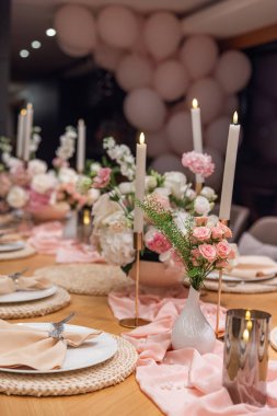 Zarif ziyafet masası, pembe çiçekli süsler, mumlar ve balon kemer süslemeleri..
