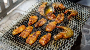 Barbekü partisi sırasında salamura pirzola ve karidesleri ızgarada pişirirken yakından bakın. Kaşık dumanlı ve sulu deniz ürünleri konseptini kullanarak yemeğin üzerine biraz baharat koy..