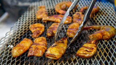 Barbekü partisinde salamura edilmiş pirzola ve karideslerin ızgarada paslanmaz çelik maşayla pişirilip takla atmasını yakından izleyin. Dumanlı ve sulu deniz ürünleri konsepti.