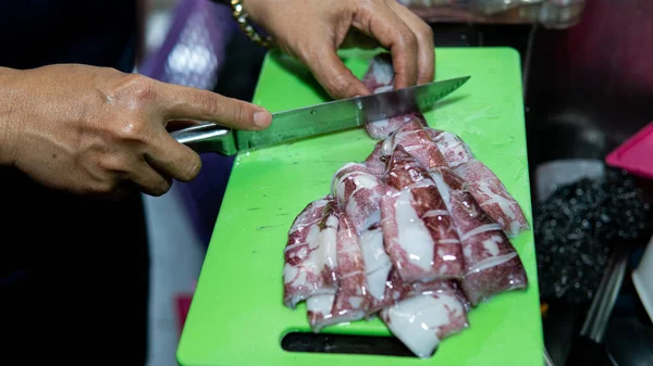 Woman hand slicing up cleaned squids using a knife on a chopping board at the kitchen. Selective focus on foregrounds.