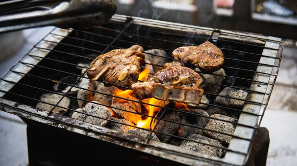 Piknik partisinde sıcak dumanlı kömür ızgarasında pişirilmiş metal maşayla sosla marine edilmiş çiğ kuzu eti tutan eli yakından izleyin. Önplanda seçmeli odak.